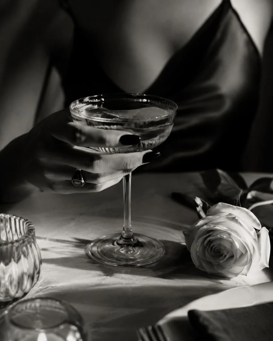 A coupe cocktail beside a white rose and candlelit marble table